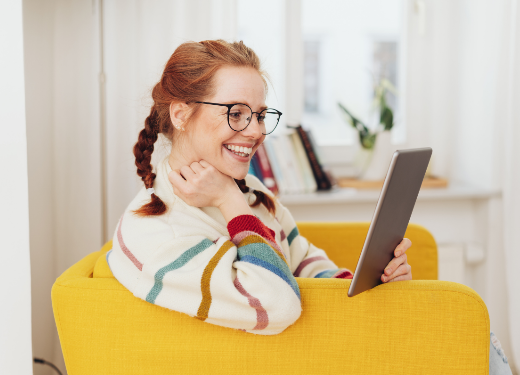 Chica joven pelirroja leyendo en una tablet mientras sonríe