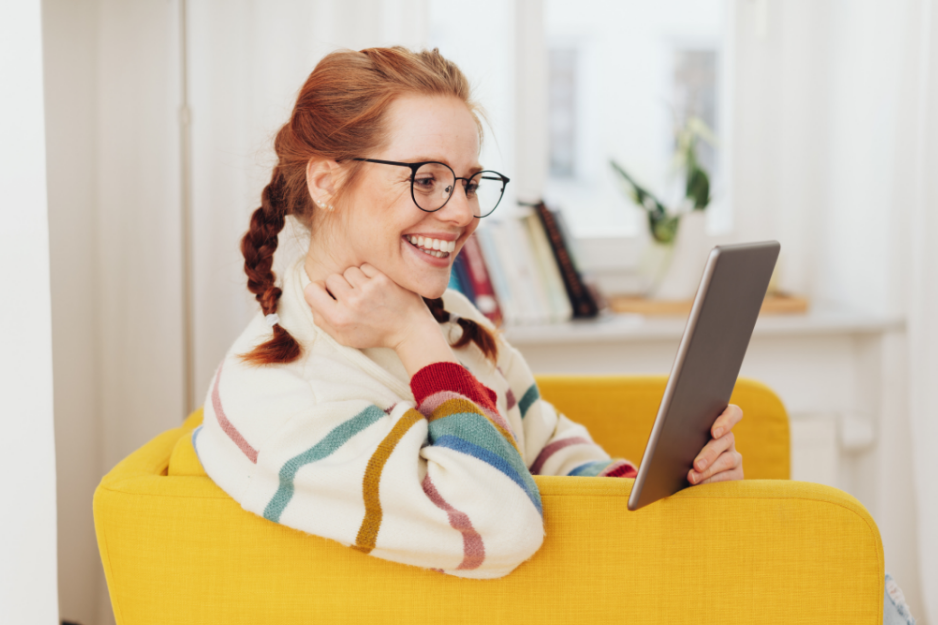 Chica joven pelirroja leyendo en una tablet mientras sonríe