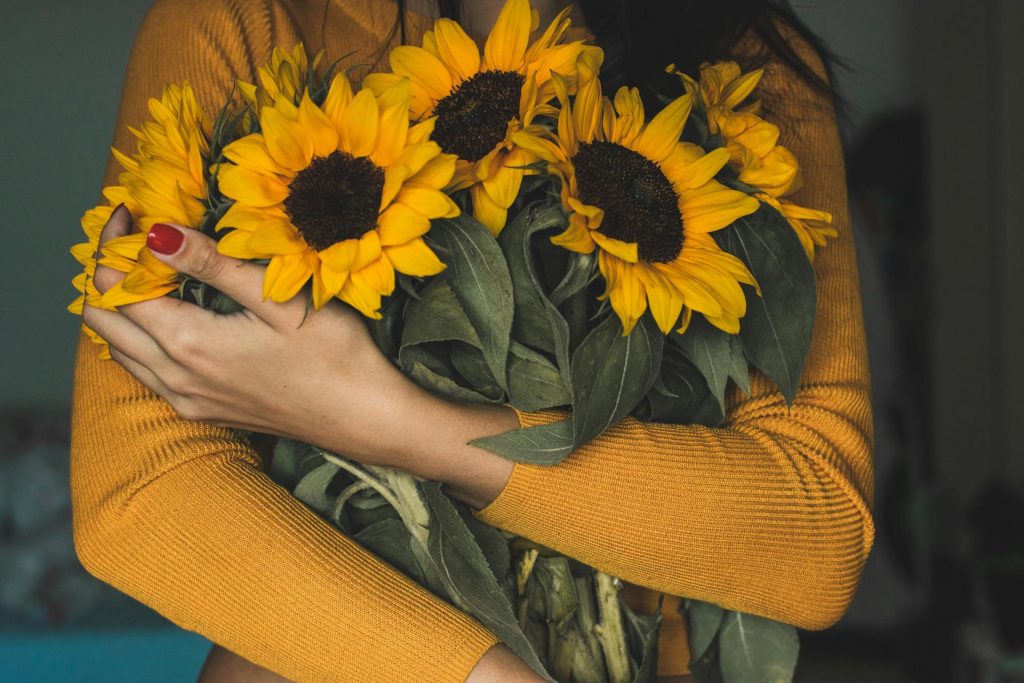 una chica abraza un ramo de girasoles. Esta imagen es parte del curso de autoestima y asertividad de Mamen Jiménez